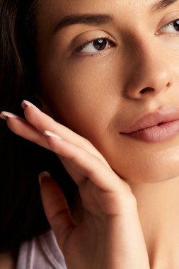 Kusursuz cilt ve kahverengi gözlerle genç dişiyi kırpın. Güzellik ve cilt bakımını görmezden gelirken nazikçe yüze dokunun.