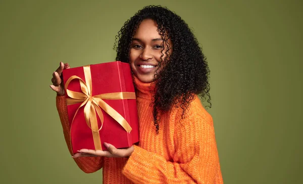 陽気なアフリカ系アメリカ人の女の子で流行のオレンジセーターに巻き毛 笑顔と開催大ギフトボックス以上緑の背景 — ストック写真