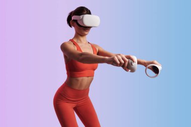 Aktif giyimli ve VR kulaklıklı formda bir bayan sporcu spor yaparken eğilim arka planına karşı kontrolörleri tutarken çömeliyor.