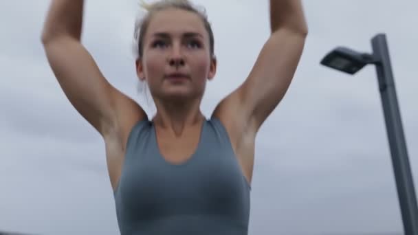 屋外でカーディオエクササイズを行うスポーツウェアの若い女性のダイナミックショットを閉じます 曇った日にジャックをジャンプするスポーティな若い女性 — ストック動画