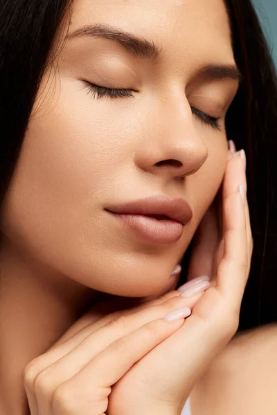 Closeup of crop brunette with perfect face skin and dark hair covering eyes and stroking skin