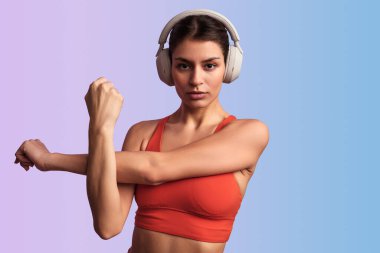 Kırmızılı kendine güvenen genç sporcu kulaklıkla müzik dinlerken arka planda spor yaparken stüdyoda ısınıyor.