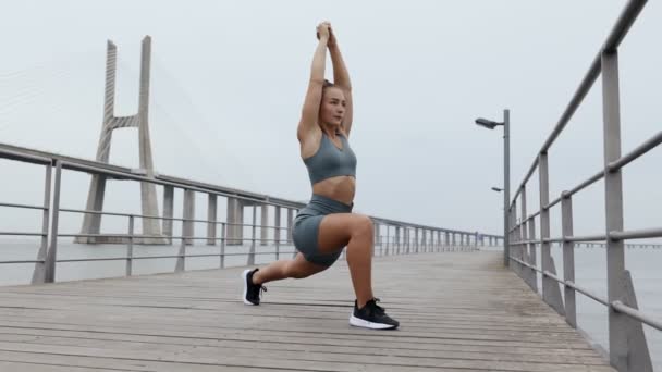 穿着运动服的女运动员在桥上做伸展运动 阴天清晨 女性以泥巴瑜伽的姿势伸展腿和手 — 图库视频影像