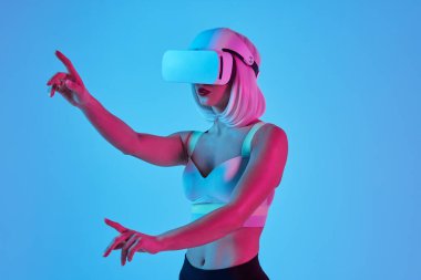 VR gözlüklü genç bir kadının mavi arka planda sanal gerçeklikle etkileşime girerken yan görüntüsü