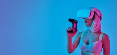 Peruklu ve VR kulaklıklı gelecekçi bayan oyuncu, neon ışıklarıyla aydınlanan stüdyoda mavi arka plandaki video oyununu kazandıktan sonra joystick 'i tutuyor.