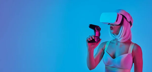 ネオンライトで照らされたスタジオで青い背景に対してビデオゲームを勝ち取った後 ウィッグとVrヘッドセットの未来的な女性ゲーマー — ストック写真