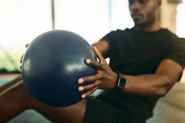 stock image Crop concentrated young African American male athlete in activewear and fitness tracker doing abs exercise with medicine ball during workout in gym