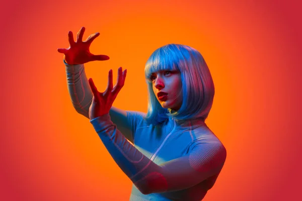 stock image Young futuristic female in cyber outfit controlling virtual interface with hands gestures against vivid neon light