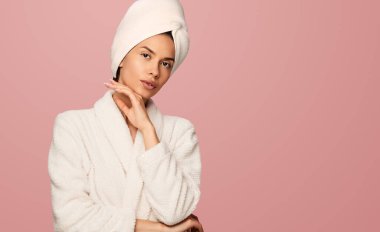 İspanyol kadın çene okşayıp kameraya bakarken banyo işleminden sonra pembe arka planda duruyor.