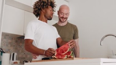 Değişik eşcinsel bir çift, afro saç stili ve kel bir erkek olan siyahi bir adam, mutfakta taze karpuz yerken sevgi dolu bir anı paylaşıyorlar.