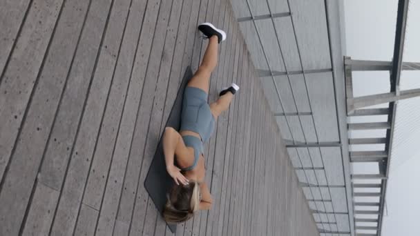 一个穿着运动服的年轻女子在室外垫子上锻炼脊椎肌肉的垂直镜头 其重点是加强背部肌肉 — 图库视频影像