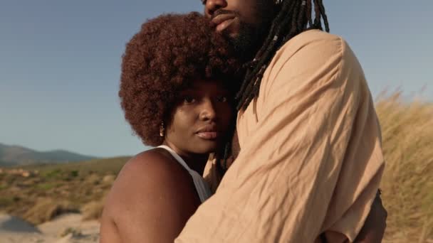 一位戴着非洲假发的非洲女性热情地拥抱着她时髦的黑人男友 在日落时分 她们在沙滩上的沙丘上分享着爱情和爱情 — 图库视频影像