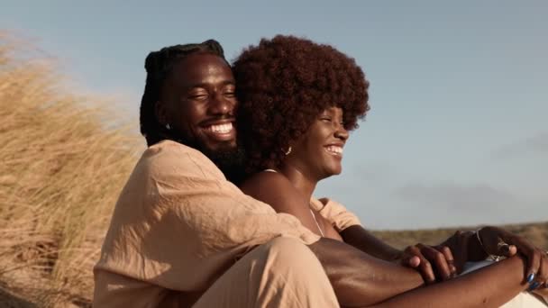 スタイリッシュなアフリカ系アメリカ人の男性と美しい女性は 日没の砂丘に愛情を抱き 笑いと会話を共有します — ストック動画