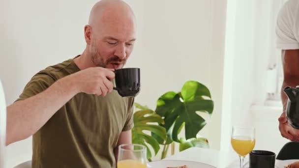 明るく照らされたアパートで一緒に朝のコーヒーを楽しむゲイカップルの心温まるシーン — ストック動画