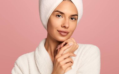 Cilt bakımından sonra kafasında havluyla güzel bir bayan pembe arka plandaki kameraya bakıyor.