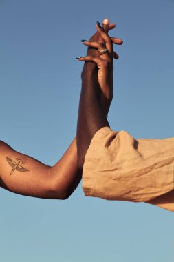 Güneşli gün desteği ve birliktelik kavramında Afrika 'lı erkek arkadaşın el ele tutuşan isimsiz dövmeli kadın.