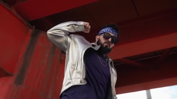 一个时髦的嘻哈男子 头戴头巾 戴着太阳镜 身穿夹克 在城市街道上桥下跳舞 — 图库视频影像