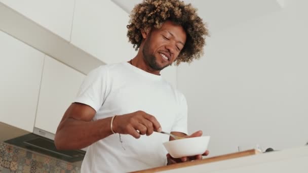 阳光明媚的早晨 一个开朗的黑色卷发男子在明亮的厨房里准备美味的煎蛋卷蛋 — 图库视频影像