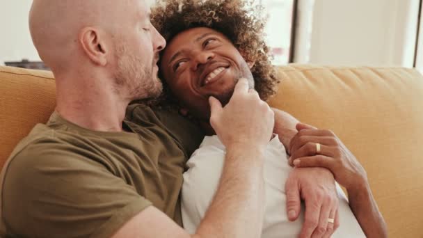 在家里舒适的沙发上 白种人和非洲的同性伴侣亲切地拥抱在一起 表达了他们的敬佩和喜悦 — 图库视频影像