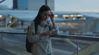 Sırt çantalı genç bir kadın akşam seyahatleri sırasında akıllı telefonuyla navigasyon haritalarını kontrol ediyor.
