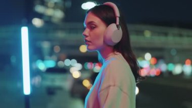 Gece şehir merkezinde akıllı telefonuyla poz veren ve kulaklık takan Z jenerasyonundan genç bir kızı etkileyen dikey bir video..