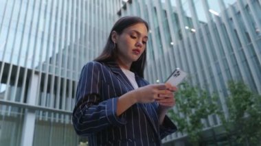 Genç bir iş kadını, bir ofis binasının zemininde akıllı telefonunu yazıp sorunları çözmek için kullanıyor.