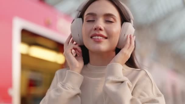 若い女性はノイズ遮断ヘッドフォンを身に着け 音楽を楽しみ 賑やかな公共交通機関の駅でタッチジェスチャーを使用しています — ストック動画