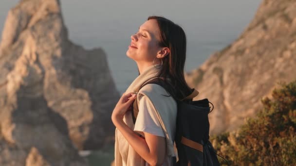 一位背着背包的年轻女子站在悬崖边上 面对美丽而美丽的海岸线 享受着新鲜的空气和大自然 — 图库视频影像