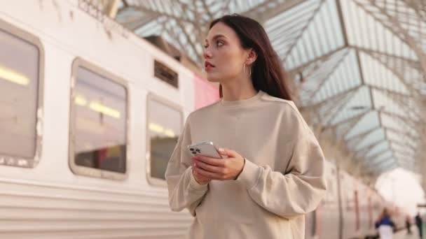 駅で彼女の列車の番号を探している若い女性 彼女のスマートフォンにデジタルチケットを保持 — ストック動画