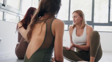 Spor giyim kuşamında üç yetişkin beyaz kadının canlı ve parlak bir stüdyo ortamında yoga dersinden önce oturup sohbet etmeleri ve iletişim kurmaları samimi bir andı.
