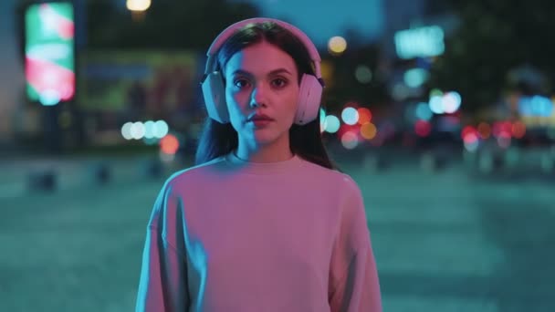 一位年轻女子沉浸在这座城市充满活力的夜生活中 在霓虹灯下戴着隔音耳机 营造出迷人的城市形象 — 图库视频影像