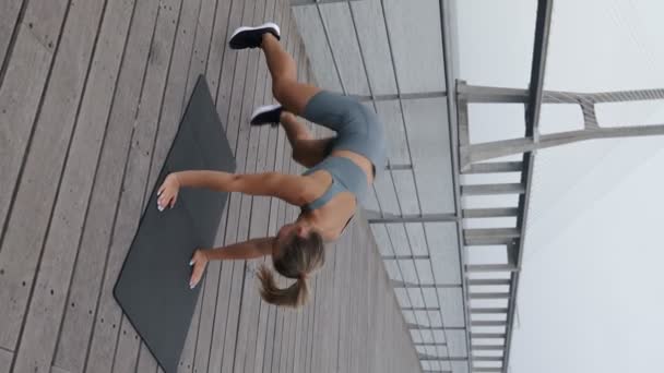年轻的女人穿着活动的衣服 在桥旁的垫子上积极地进行户外运动 俯卧撑和隆隆起跳 培养力量 敏捷性和健康的生活方式 — 图库视频影像