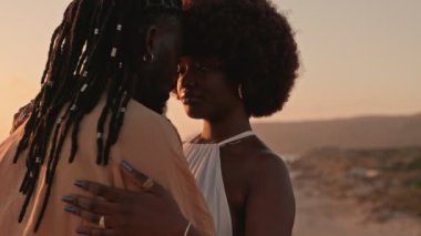 Yakından çekilen bir fotoğraf şık bir Afrikalı siyahi çiftin samimi anını yakalıyor. Birbirlerine sarılıyorlar ve güzel bir günbatımı arka planına bakıyorlar.
