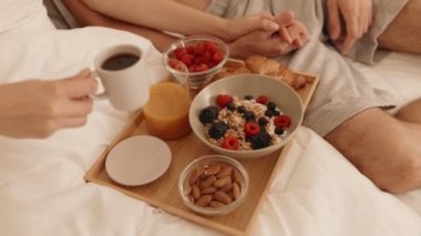 Müsli, yoğurt, kruvasan, ahududu ve meyve suyu içeren bir tepsinin yakın çekimi ile keyifli bir sabah geçiren bir çift.