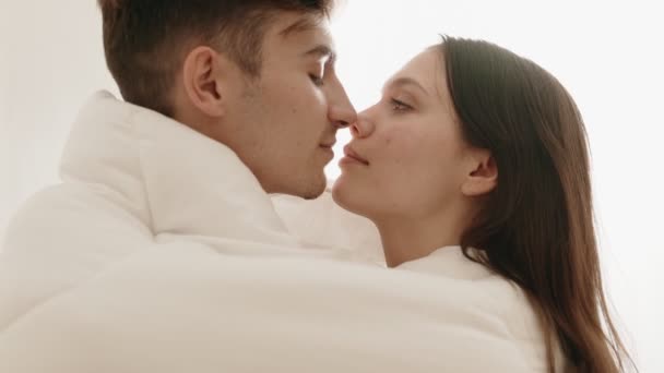 居心地の良い毛布の下で情熱的なキスを共有する美しい若い白人カップルのハイキーサイドビュークローズアップ — ストック動画