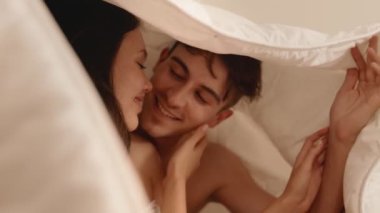 Romantik bir an tatlı bir çiftin şefkatli bir öpücüğü paylaşıyor ve sıcak bir battaniyenin altında sarılıyor.