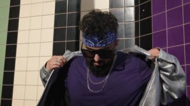 Tarz sahibi genç bir adam modaya uygun ceketini şehir duvarına, sokak kıyafetlerine ve güneş gözlüklerine göre ayarlıyor.