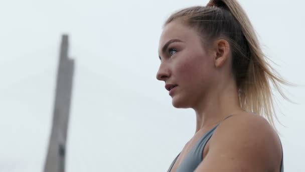 決定された若い女性は魅惑的な空の背景に対する彫刻された肩の筋肉のための焦点を合わせたダンベル前部上昇を行います — ストック動画