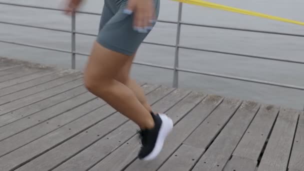 一位20多岁的无法辨认的年轻女子在海滨带着一支抵抗带进行着锻炼 表现出了健身的决心和决心 — 图库视频影像