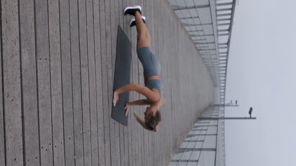 年轻女子在海滨长廊上活动穿便服 独自一个人在多云的日子里用手托着身体 锻炼体力 — 图库视频影像