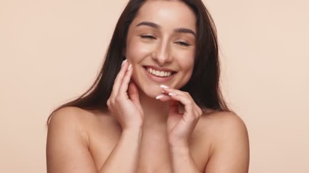 完璧な肌で陽気な若いアルメニア人女性のクローズアップ 笑顔と彼女の顔に優しく中立的な背景に触れる — ストック動画