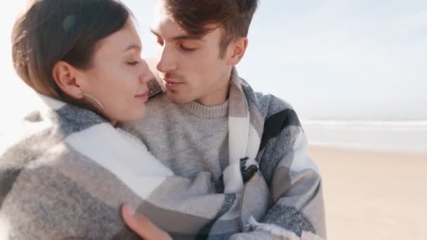 若いカップルのキスとして捉えられたロマンチックな瞬間は ビーチの居心地の良い毛布に包まれ 背景の海で — ストック動画