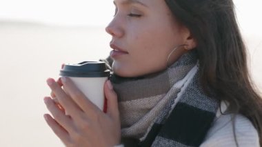 Soğuk bir günde sıcak bir kahve fincanının sıcaklığının tadını çıkaran 20 'li yaşlarındaki genç bir kadının rahat ve rahatlatıcı bir görüntüsü..