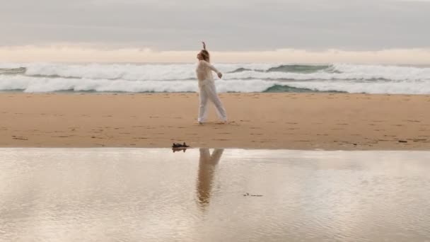 白い20代の若い女性は 日没に閉ざされたビーチで単独で現代的なダンスを行います イメージは 海に対する自由 そして動きの美しさを描いています — ストック動画