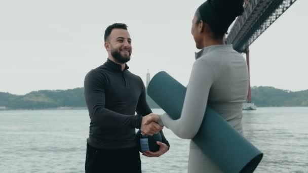 Two Happy Fitness Enthusiasts Exercise Mat Shaking Hands Embrace Waterfront — Stock Video