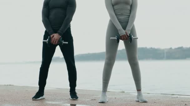 スポーツのフィットネストレーナーと黒人の若い女性のトレーニングは 川沿いのウェアリフトウェイトを着用し 背中の筋肉のためのチームワーク および屋外フィットネスを紹介しています — ストック動画