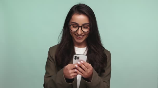 一个快乐的年轻女人 戴着眼镜 看着智能手机屏幕 带着枯燥无味的背景音乐微笑着发短信 传达着快乐和联系 — 图库视频影像