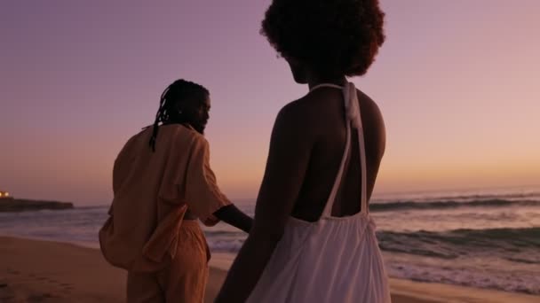 在美丽的落日下 一对身穿时髦服装的非洲年轻夫妇在海滩上散步 展示了他们的爱情和融合的轮廓 — 图库视频影像