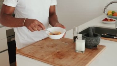 Beyaz bir kâsede yumurta çırpan, güneşli bir günde şık bir mutfakta ev yapımı omlet hazırlayan siyah bir adamın yakın çekimi..