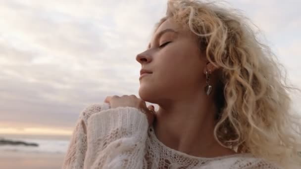 一个安静的年轻女子 闭着眼睛 呼吸着大海的新鲜空气 夕阳西下 天空一片温暖 — 图库视频影像